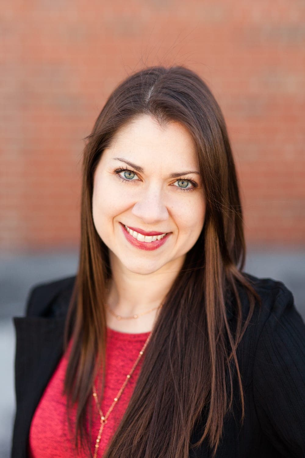Jennifer Widmer, Ottawa County Auditor, smiling in a red top and dark blazer against a brick wall